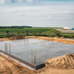 Fotografia przedstawiająca plac budowy z wykopanymi rowami i wylanymi ławami fundamentowymi.