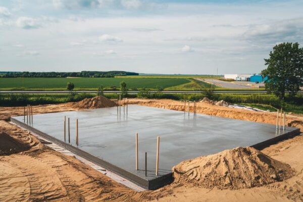 Fotografia przedstawiająca plac budowy z wykopanymi rowami i wylanymi ławami fundamentowymi.